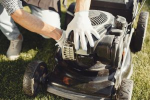 Man Cutting Grass With Lawn Mower Back Yard Male Black Apron Guy Repairs